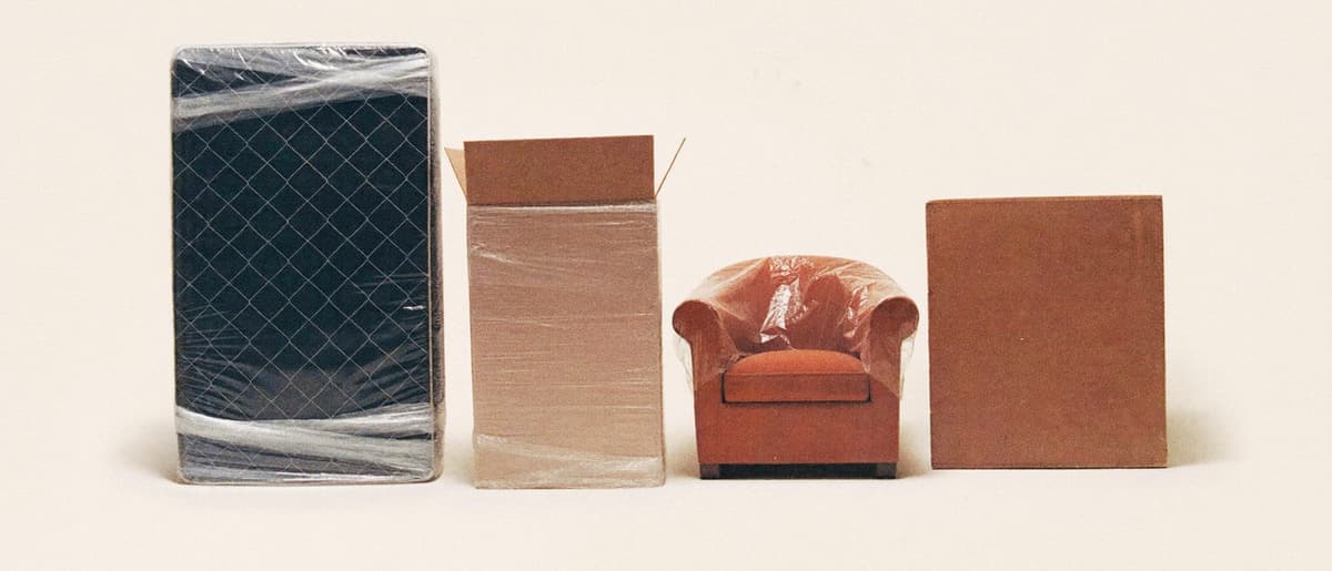 Colchón, heladera, sillón y muebles embalados, alineados sobre fondo crema.
